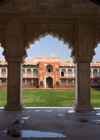 Private courtyard seen from under arches of Palace at Agra Fort in India. Green grounds, blue skies, beige arches frame red gate and white gallery.のeditorial素材
