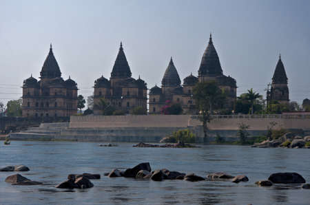 Tall beige brown mausoleum structures with similar domes over blue rocky water.のeditorial素材