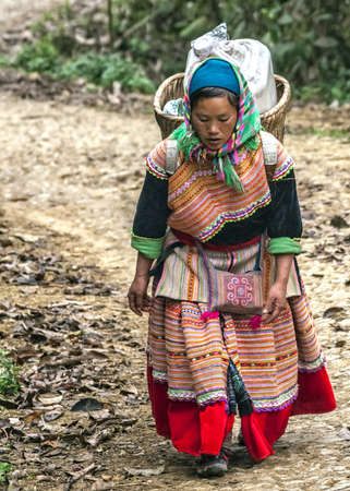 Hmong woman with loaded basket on her back comes around the bend in the road. Colorful appearance.のeditorial素材