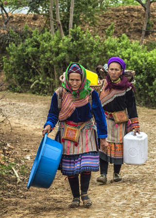 Two Hmong women loaded up baskets on their backs come around the bend in the road. Colorful appearance.のeditorial素材