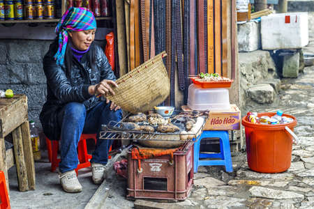 Cat Cat. Vietnam  - March 3, 2012: Hmong woman disperses smoke of primitive roast pit.のeditorial素材