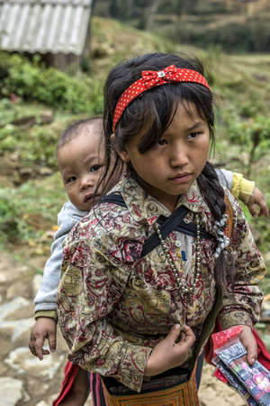 Cat Cat, Vietnam - March 10, 2012: Young girl with baby on her back peddles.のeditorial素材