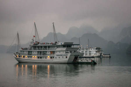 Halong Bay, Vietnam  - March 13, 2012: Cruise junk boat sitting under early morning fog in front of limestone mountains. Mysterious romantic peaceful scenery out of fairytale.のeditorial素材