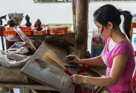 Young woman in pink shirt rolling incense sticks.のeditorial素材