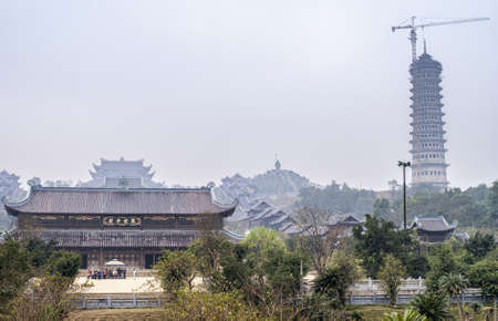 Grey morning skies over Pagoda buildings, giant Buddha statue in the far distance and new tower under construction.のeditorial素材