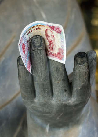 Vietnam Chua Bai Dinh Pagoda, one colorful Dong note held by granite hand.