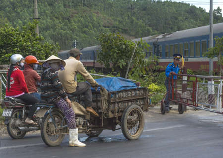 Central Vietnam - March 2012: The guard closes the railway fence to let the train pass, while motorbike riders wait.のeditorial素材