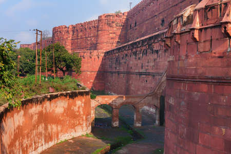 Red ramparts and empty moat of Agra Fort in India  Huge thick defensive wall with battlements on top, and green on other side of the moat のeditorial素材