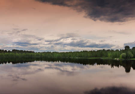 A green ribbon divides the colorful skies from the lake that reflects the strange menacing sky.の写真素材