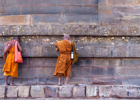 SARNATH, INDIA - CIRCA FEBRUARY 2011  Two Buddhist monks talking to the Dhamekh Stupa, while leaning against the wall, partly covered with gold のeditorial素材