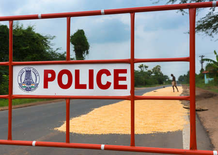 Tamil Nadu Police barrier protects drying corn on the public road, alerting traffic to drive around the patch of grain.のeditorial素材