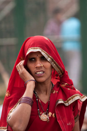 DELHI, INDIA - FEBRUARY 6, 2011: closeup of Hindu woman holding her red head scarf with her right hand as if she makes a phone call. She wears plenty of jewelry.のeditorial素材