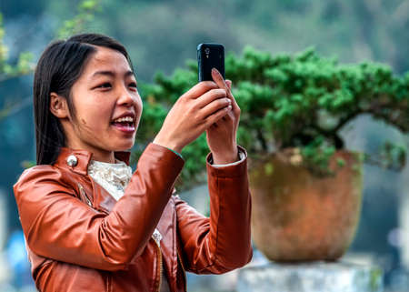 HANOI, VIETNAM - MARCH 6, 2012: A young Vietnamese woman wearing a leather vest takes a picture with her smart phone.のeditorial素材