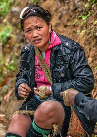 CAT CAT, VIETNAM - MARCH 9, 2012: Young Hmong woman twists strings using her both hands while sitting on the side of the road.のeditorial素材