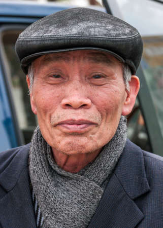 VINH, VIETNAM - MARCH 15, 2012: Closeup of older Vietnamese man with gray-black had and a thick shawl under his jacket.のeditorial素材