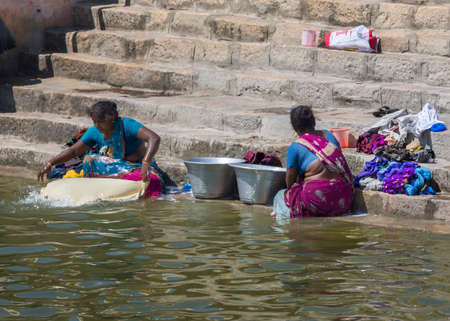 KUMBAKONAM, INDIA - OCTOBER 11, 2013: Two women are doing laundry on the steps of the sacred Maha Maham tank downtown. They are wading into the water.のeditorial素材