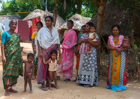 KUMBAKONAM, INDIA - OCTOBER 11, 2013: A group of women of different ages look after the youngest children. Their straw-roof houses and huts stand in the background and so does hanging laundry.のeditorial素材