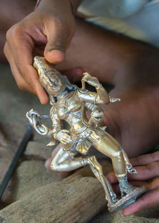 KUMBAKONAM, INDIA - OCTOBER 11, 2013: Closeup of hands holding the metal statue that came out of the clay mold. Tiny pieces of clay must now be removed out of crevices and nooks. Supports must be filed off.のeditorial素材