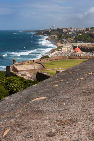 SAN JUAN, PUERTO RICO - MARCH 14, 2015: View from the ramparts of Castillo San Felipe del Morro to the east: the Atlantic Ocean, Part of ramparts, Cemetery Santa Maria Magdalena, La Perla bario and beyond under a blue sky.のeditorial素材