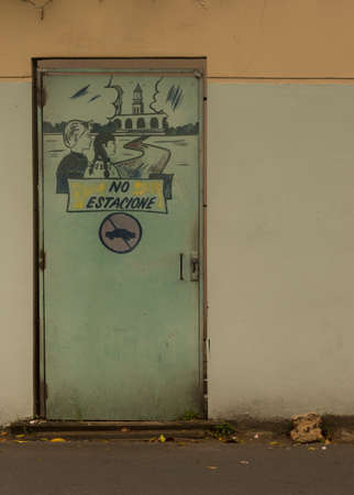 SAN JUAN, PUERTO RICO - MARCH 7, 2015: Graffiti in Rio Piedras neighborhood. Sign saying not to park a car here. Image shows young man and young woman looking at the Roosevelt bell tower of the university. Wall is yellow. Door is light green.のeditorial素材