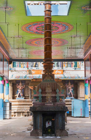 KUMBAKONAM, INDIA - OCTOBER 12, 2013: Mahalingeswarar Temple. An open-sided hall or walkway leads to the inner sanctum. The tall, copper flagpole reaches through the painted ceiling. A blackened Ganesha shrine fronts it. Two Dwarapalakas, door keepers of のeditorial素材