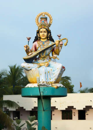KUMBAKONAM, INDIA - OCTOBER 12, 2013: The goddess Saraswathi sits on a circular platform fixed on a single pole. Statue in front of school along the rural road against a light blue sky. Sheâs the goddess of education and plays the Veena instrument.のeditorial素材