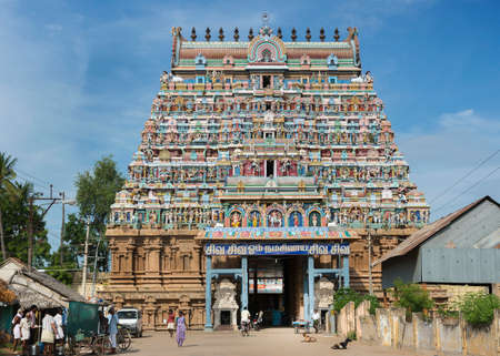 KUMBAKONAM, INDIA - OCTOBER 12, 2013: Mahalingeswarar Temple. The tall, pastel-colored Gopuram above the main entrance to this very large Shiva temple. The entire tower is filled with religious statues. Blue sky. A few people and goats in front of the temのeditorial素材