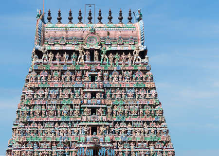 KUMBAKONAM, INDIA - OCTOBER 13, 2013: Top half Gopuram of the Kumbeswarar temple against blue sky. Rows above rows of pastel colored statues, crowned by the Kumbam, the apex.のeditorial素材