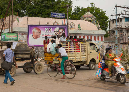 Thanjavur, India - October 15, 2013: A construction crew, males and females, is transported standing in the loading area of pickup truck to their job. Concrete mill trails the truck. Street scene shows bike and moped.のeditorial素材