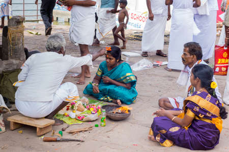 Trichy, India - October 15, 2013: Religious ritual to promote conceiving and pregnancy at Amma Mandapam. Offerings have been made, a flame has been lighted and family members watch. Here, the guru touches the head of the young woman with an orange, simpliのeditorial素材