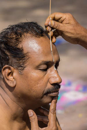 Trichy, India - October 15, 2013: Closeup of mans face while a guru paints the Vishnu symbol in...