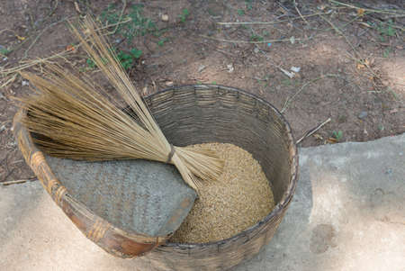 Chettinad, India - October 16, 2013: Near Namunasamudran, a reed-woven basket filled with fresh-harvested rice stands on the road. Stalks from a broom and lie on a woven scoop.の写真素材