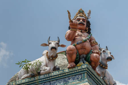Chettinad, India - October 17, 2013:Detail of the Shiva temple at Kottaiyur shows half-naked Ayyanar on wall in company of two bulls against blue sky.のeditorial素材