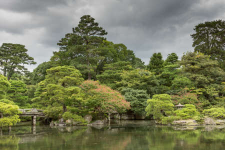 Kyoto, Japan - September 14, 2016: Part of the Japanese garden at the imperial palace showing bridge, pond, trees and flowers under heavy sky.のeditorial素材