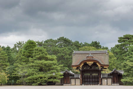 Kyoto, Japan - September 14, 2016: The charming Kenshun-mon gate stands between a row of green trees under heavy skies. Wood carvings and golden trim.のeditorial素材