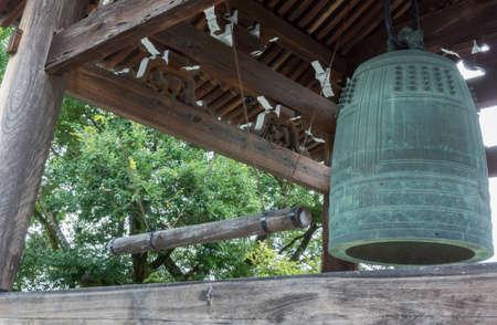 Kyoto, Japan - September 15, 2016: The giant, green metal bell hangs in pagoda at Kurodani Buddhist Temple. Dark brown wood structure and some green trees.のeditorial素材