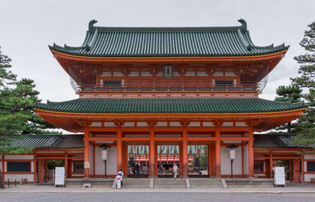 Kyoto, Japan - September 15, 2016: Monumental vermilion entrance gate of the Heian Shinto Shrine. Green roof in Japanese style. Gray skies. People walk up the steps.のeditorial素材