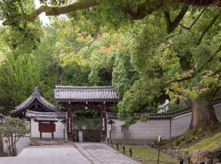 Kyoto, Japan - September 16, 2016: The humble entrance gate to the Shorenin Buddhist Temple is set at the edge of a formal garden with large trees. Pay gray wall and dark wooden structure.のeditorial素材