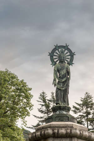 Kyoto, Japan - September 16, 2016: Quan Yin standing in lotus and with halo statue on pedestal in Yuzen-en garden of Chion-in Buddhist Temple. Cloudy skies, some green trees.のeditorial素材