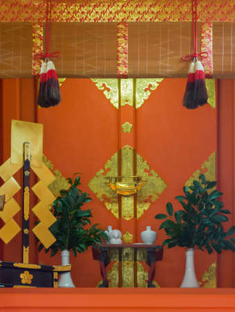 Kyoto, Japan - September 17, 2016: Altar of small shrine at Fushimi Inari Taisha Shinto Shrine offers a dominant vermilion color with golden decorations, white vases and green leaves.のeditorial素材