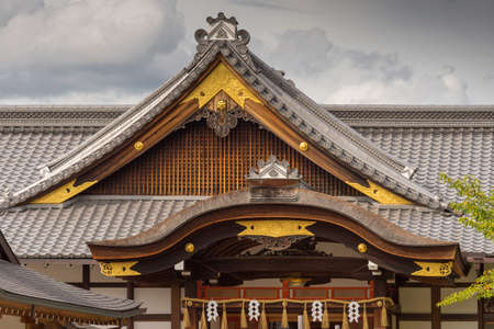 Kyoto, Japan - September 17, 2016: Two different shapes of roof structure at Fushimi Inari Taisha Shinto Shrine. Gray tiles, brown facial boards and golden trim under cloudy skies.のeditorial素材