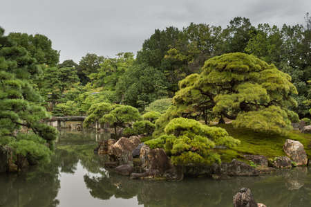 Kyoto, Japan - September 19, 2016: View on part of the garden of Ninomaru Palace at Nijo Castle. Pond, rocks, trees and a small bridge. Cloudy sky.のeditorial素材