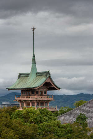 Kyoto, Japan - September 19, 2016: The pagoda of Daiunin Buddhist temple towers over trees under cloudy sky. The Phoenix stands on top of sharp, long, green peak and roof. Hills and jungle in background.のeditorial素材