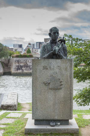 Hiroshima, Japan - September 20, 2016: One half of the Literature Monument in honor of the Japanese writer Miekichi Suzuki. Granite slab with statue of his bust and him holding peace pigeons at Peace Memorial Park in Hiroshima.のeditorial素材