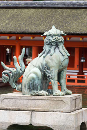 Hiroshima, Japan - September 20, 2016: Closed mouth lion statue at itsukushima Shinto Shrine on Miyajima Island. Vermilion wood structures in back. Shrine is built on platforms in Inland Sea.のeditorial素材