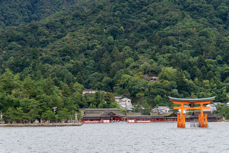 Hiroshima, Japan - September 20, 2016: Iconic vermilion Torii in front of Itsukushima Shinto Shrine set against the jungle top hill on Miyajima Island. Seen from on the Inland Sea.のeditorial素材
