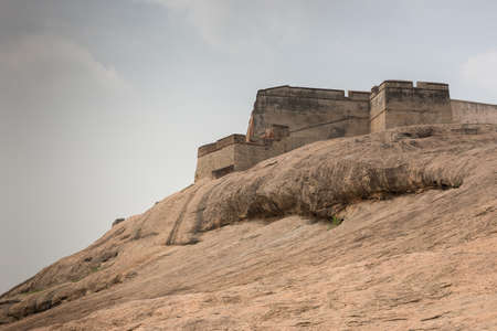 Dindigul, India - October 23, 2013: Brown-beige boulder with the ramparts of the historic Dindigul Rock fort under light blue sky. Brown-beige as dominant color.のeditorial素材