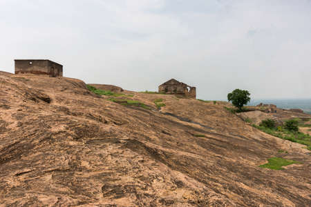 Dindigul, India - October 23, 2013: Brown-beige boulder plain inside historic Dindigul Rock Fort. Two ruins and a tree dispersed in landscape. Light blue sky.のeditorial素材