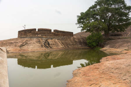 Dindigul, India - October 23, 2013: A short dam creates an artificial pond to collect rain water inside Dindigul Rock Fort. One lone tree and fortifications.のeditorial素材