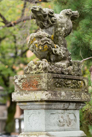Kanazawa, Japan - September 22, 2016: Old stone Japanese Lion-monster statue at Kenrokuen Garden functions as guardian. Beast throws back legs in air. Moss and yellow mold. Green foliage as background.のeditorial素材